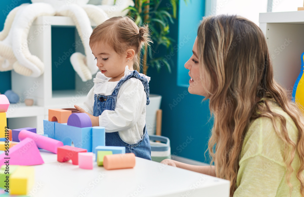 Teacher and toddler playing with geometry blocks sitting on table at kindergarten Teacher and toddler playing with geometry blocks sitting on table at kindergarten