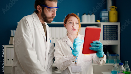 Man and woman wearing sciencist uniform using touchpad at laboratory