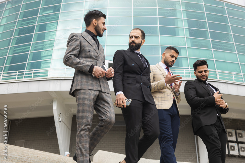 Business people outdoor meeting. A group of male businessmen in suits walk down the street stairs against the backdrop of a glass building. Working break. Teamwork and brainstorming. Business people outdoor meeting. A group of male businessmen in suits walk down the street stairs against the backdrop of a glass building. Working break. Teamwork and brainstorming.