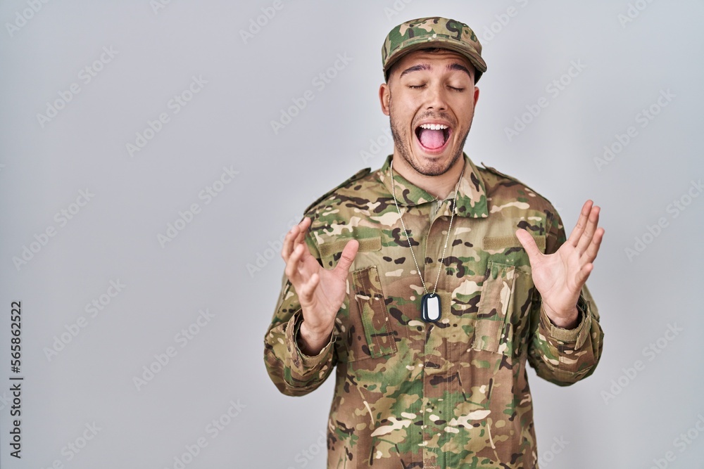 Young hispanic man wearing camouflage army uniform celebrating mad and crazy for success with arms raised and closed eyes screaming excited. winner concept Young hispanic man wearing camouflage army uniform celebrating mad and crazy for success with arms raised and closed eyes screaming excited. winner concept