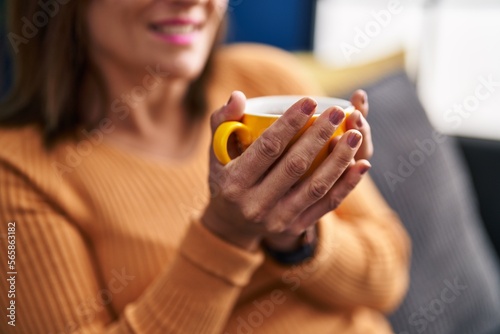 Middle age woman drinking coffee sitting on sofa at home