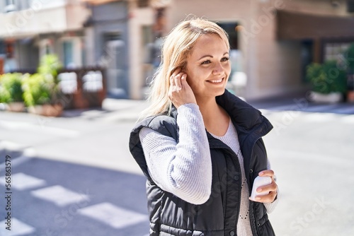 Young blonde woman listening to music at street