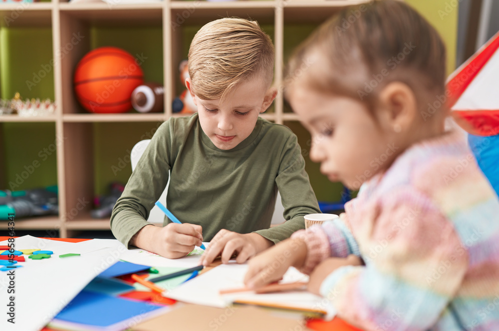 Fototapeta premium Two kids preschool students sitting on table drawing on paper at kindergarten