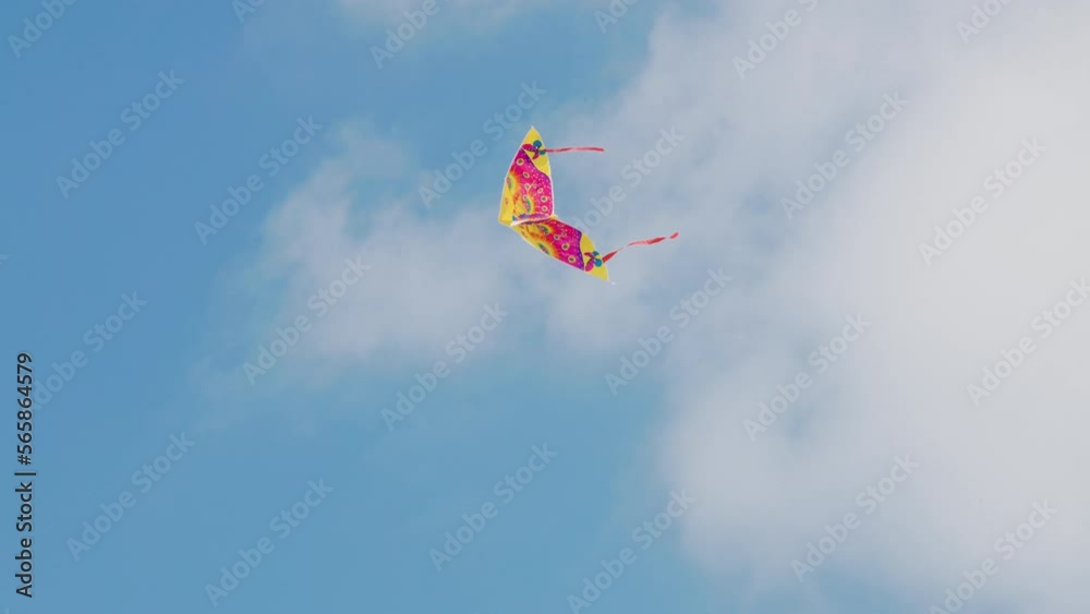 Colorful kite flying in the blue sky under gusts of wind with some white clouds up high. Hobbies and leisure activities concept. 4k Footage.