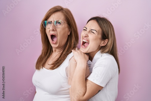 Hispanic mother and daughter wearing casual white t shirt angry and mad screaming frustrated and furious, shouting with anger. rage and aggressive concept.