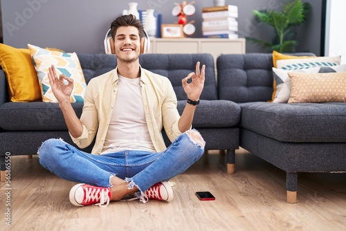 Young hispanic man doing yoga exercise sitting on floor at home
