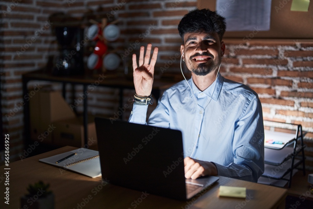 Young hispanic man with beard working at the office at night showing and pointing up with fingers number four while smiling confident and happy. Young hispanic man with beard working at the office at night showing and pointing up with fingers number four while smiling confident and happy.