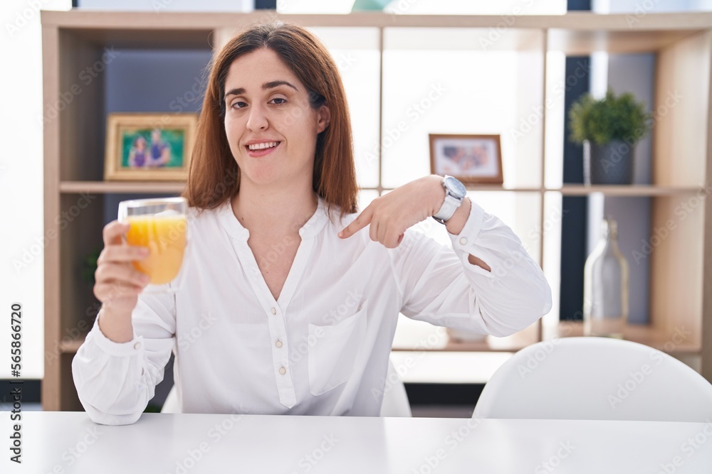 Brunette woman drinking glass of orange juice looking confident with smile on face, pointing oneself with fingers proud and happy. Brunette woman drinking glass of orange juice looking confident with smile on face, pointing oneself with fingers proud and happy.