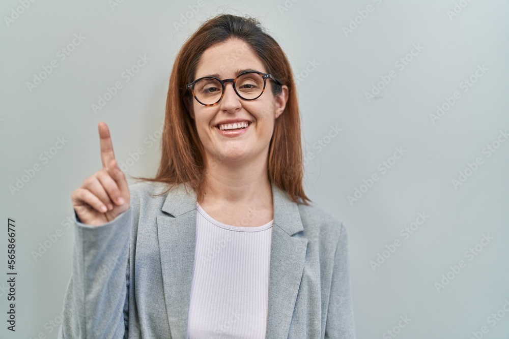 Brunette woman standing over grey background smiling with an idea or question pointing finger up with happy face, number one Brunette woman standing over grey background smiling with an idea or question pointing finger up with happy face, number one