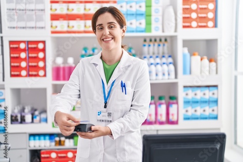 Young woman pharmacist holding pills using credit card and dataphone at pharmacy
