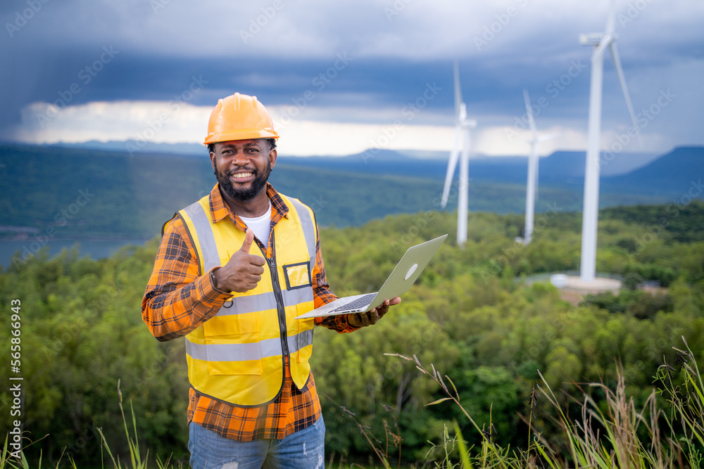 Portrait of engineer African American man working with laptop in wind turbine farm.