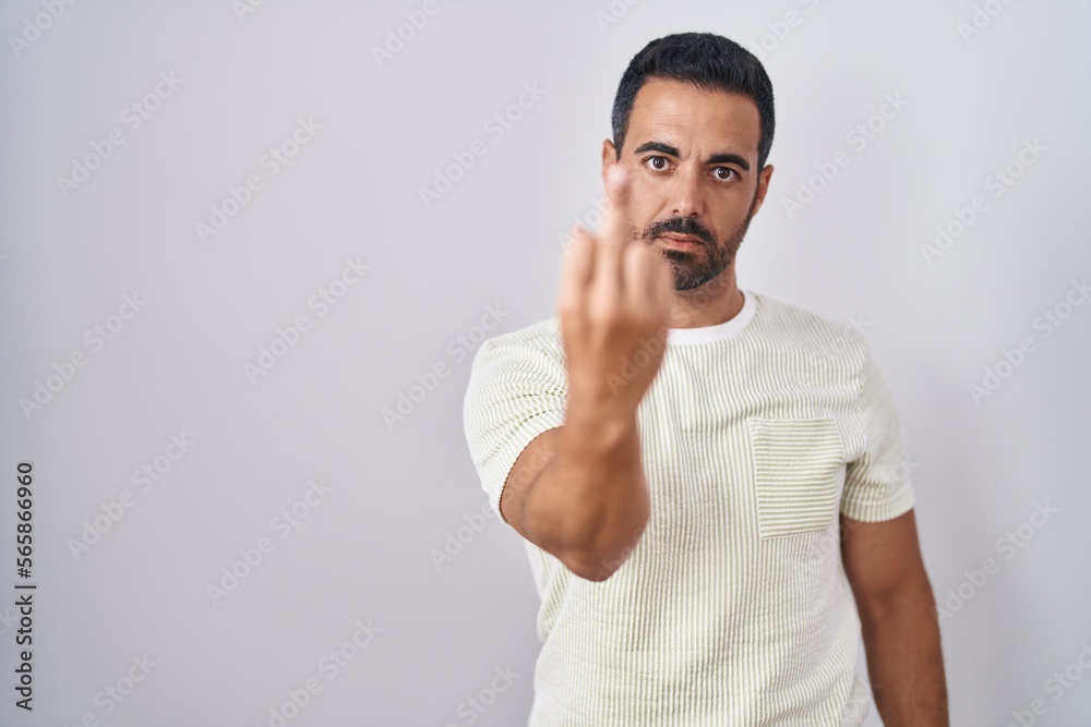 Hispanic man with beard standing over isolated background showing middle finger, impolite and rude fuck off expression Hispanic man with beard standing over isolated background showing middle finger, impolite and rude fuck off expression