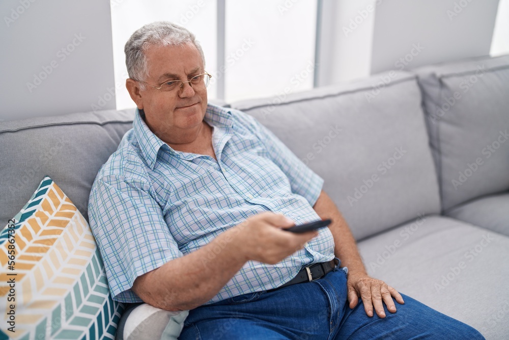 Middle age grey-haired man watching television sitting on sofa at home Middle age grey-haired man watching television sitting on sofa at home