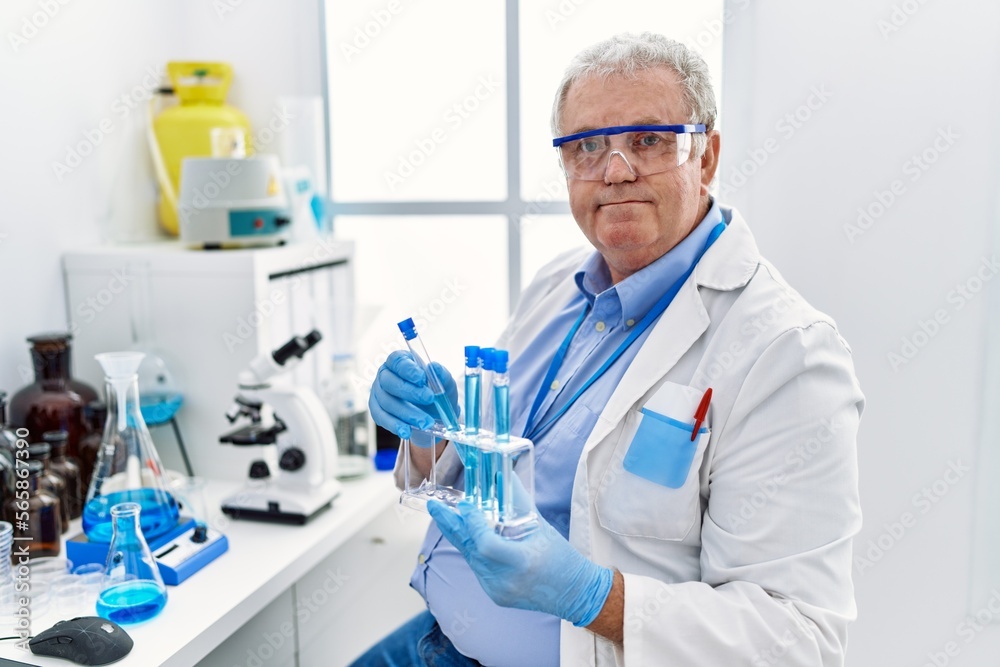 Middle age grey-haired man wearing scientist uniform holding test tube at laboratory Middle age grey-haired man wearing scientist uniform holding test tube at laboratory