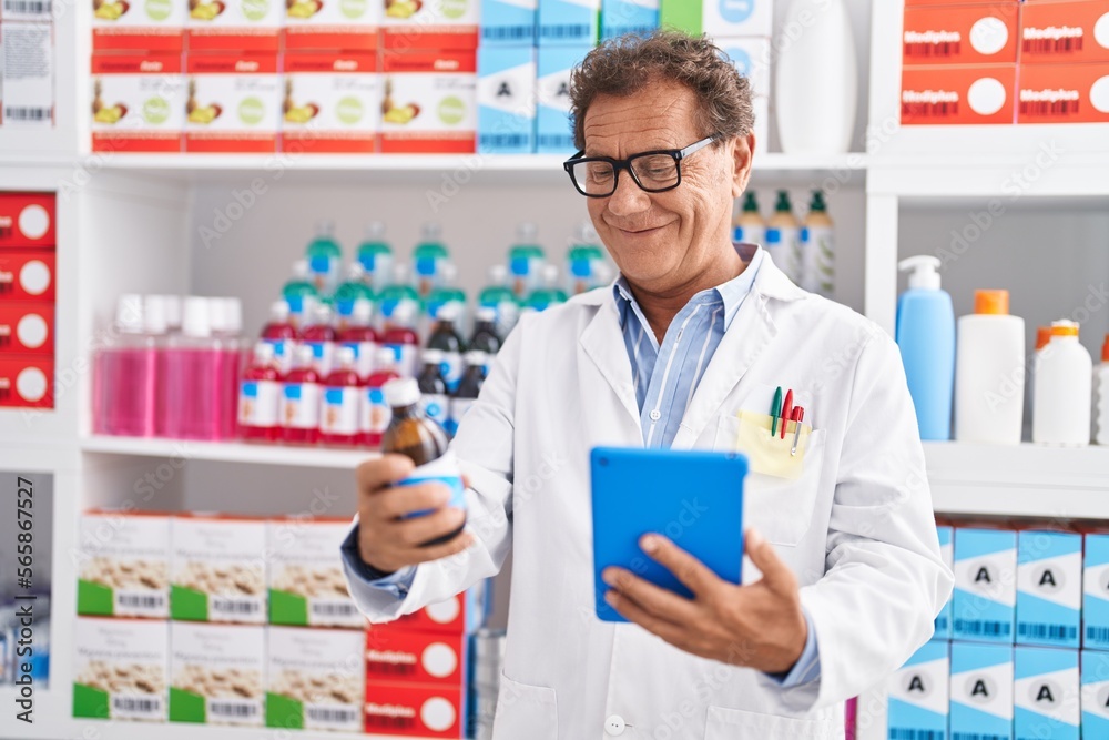 Middle age man pharmacist using touchpad holding medicine bottle at pharmacy