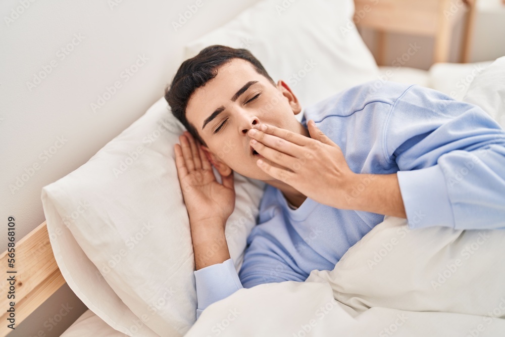 Young non binary man lying on bed yawning Young non binary man lying on bed yawning