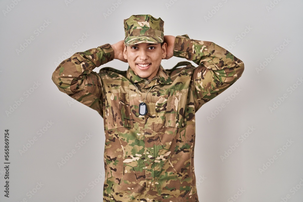 Young arab man wearing camouflage army uniform relaxing and stretching, arms and hands behind head and neck smiling happy Young arab man wearing camouflage army uniform relaxing and stretching, arms and hands behind head and neck smiling happy