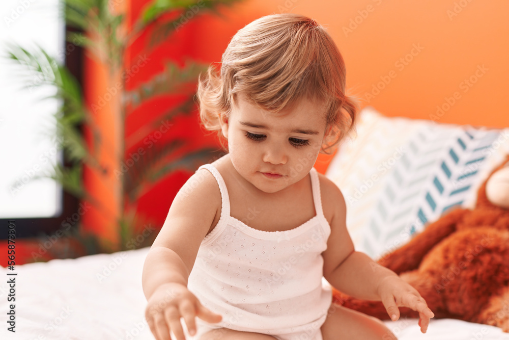 Fototapeta premium Adorable hispanic toddler sitting on bed with relaxed expression at bedroom