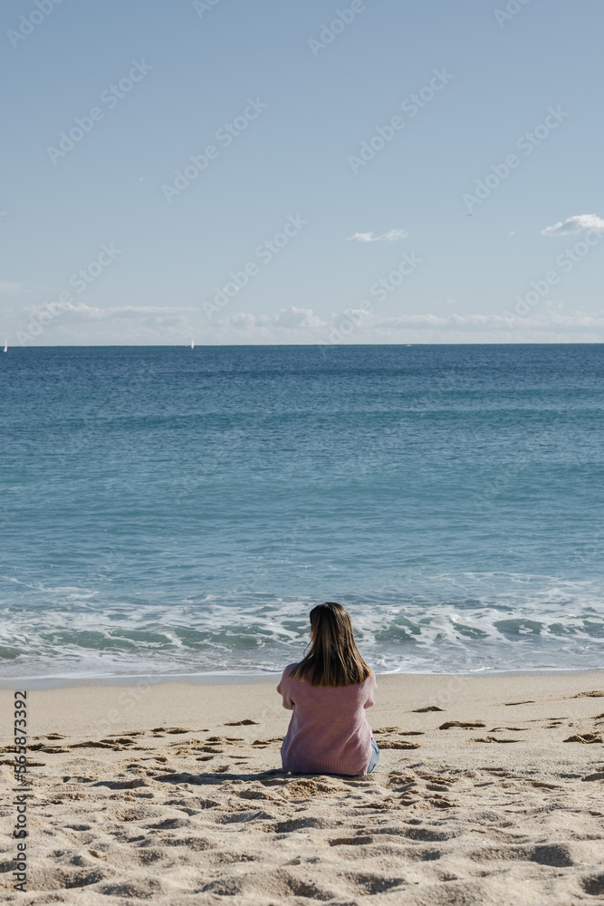 Woman sitting on the beach looking at the sea.