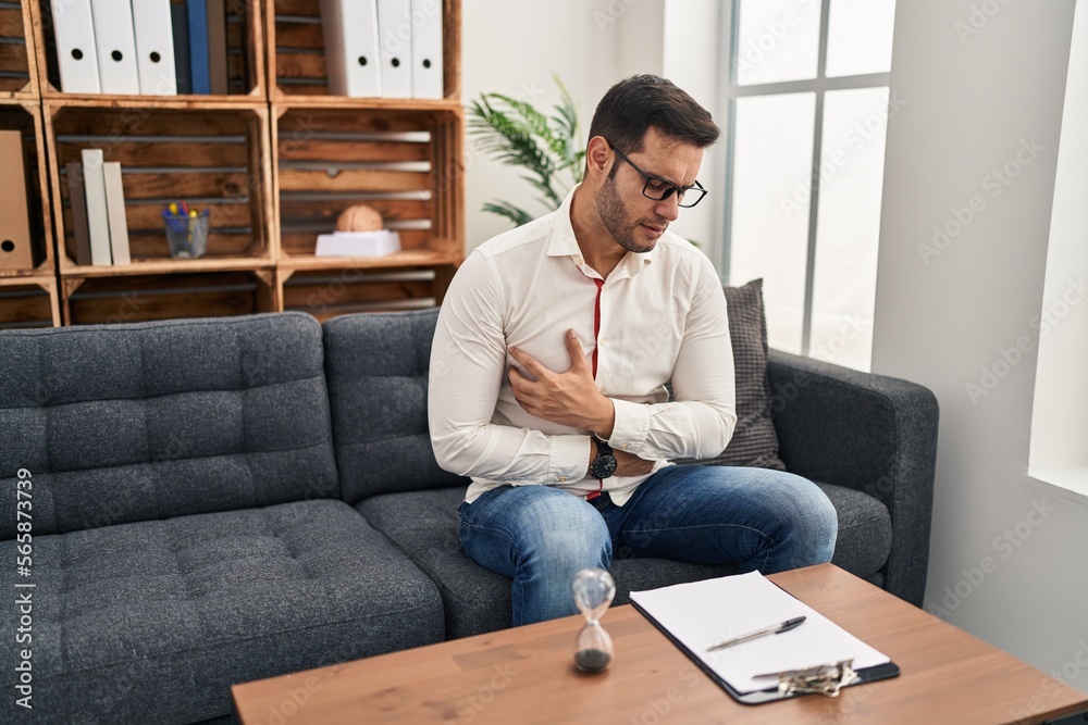 Young hispanic man with beard working at consultation office with hand on stomach because indigestion, painful illness feeling unwell. ache concept. Young hispanic man with beard working at consultation office with hand on stomach because indigestion, painful illness feeling unwell. ache concept.