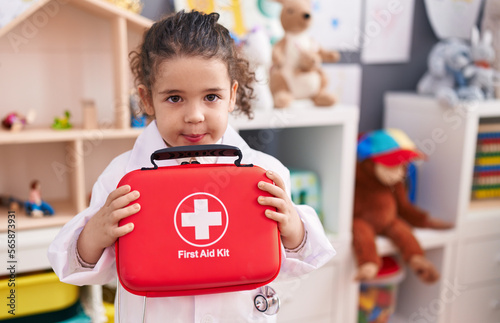 Adorable hispanic girl wearing doctor uniform holding first kit aid at kindergarten photo