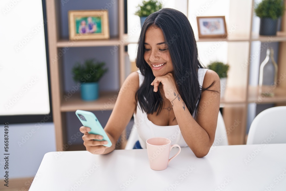 Young hispanic woman drinking coffee and using smartphone at home Young hispanic woman drinking coffee and using smartphone at home
