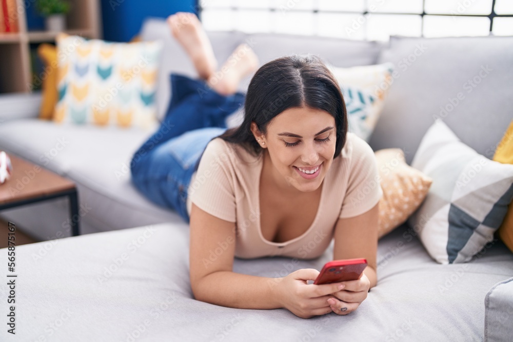 Young beautiful hispanic woman using smartphone lying on sofa at home Young beautiful hispanic woman using smartphone lying on sofa at home
