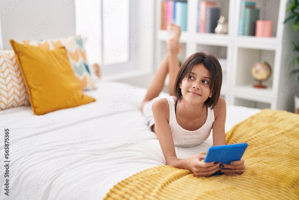 Adorable hispanic girl using touchpad sitting on bed at bedroom Adorable hispanic girl using touchpad sitting on bed at bedroom