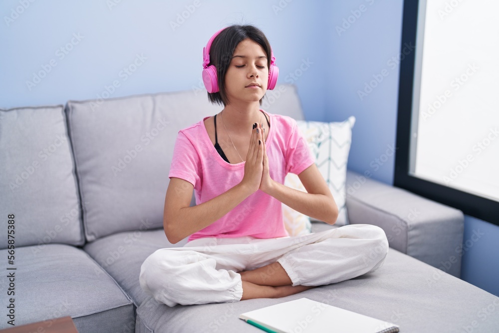 Adorable hispanic girl doing yoga exercise sitting on sofa at home Adorable hispanic girl doing yoga exercise sitting on sofa at home