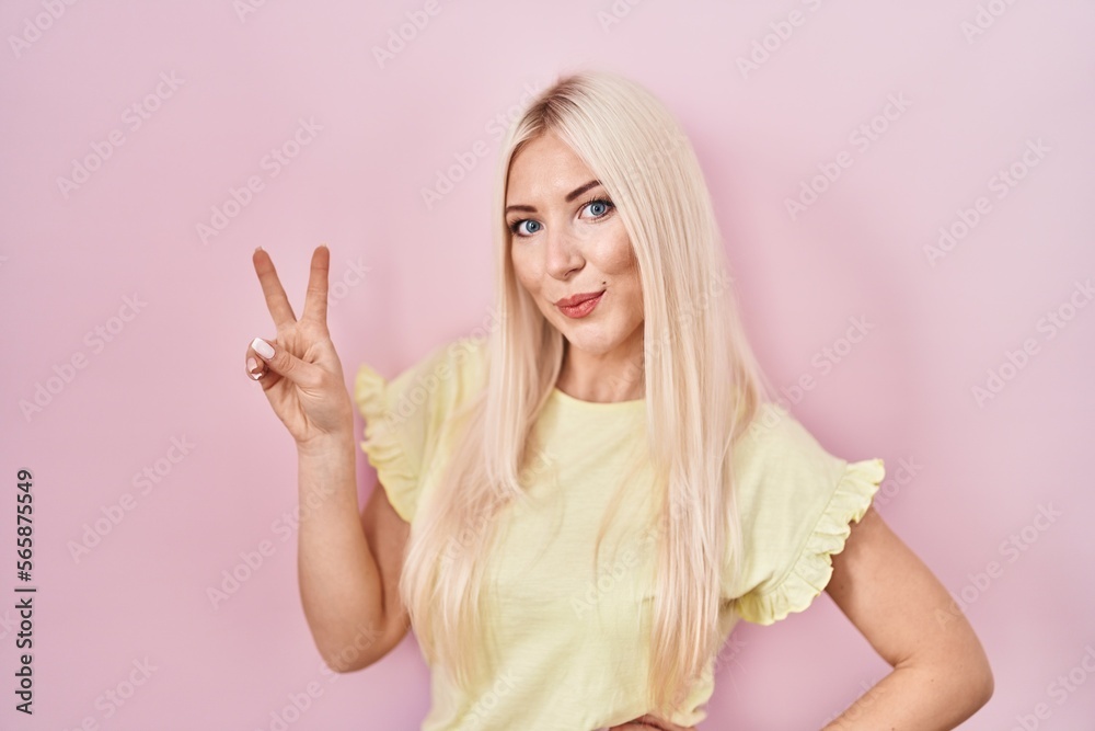 Caucasian woman standing over pink background smiling looking to the camera showing fingers doing victory sign. number two. Caucasian woman standing over pink background smiling looking to the camera showing fingers doing victory sign. number two.