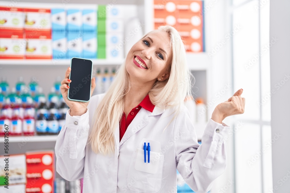 Caucasian woman working at pharmacy drugstore showing smartphone screen screaming proud, celebrating victory and success very excited with raised arms Caucasian woman working at pharmacy drugstore showing smartphone screen screaming proud, celebrating victory and success very excited with raised arms