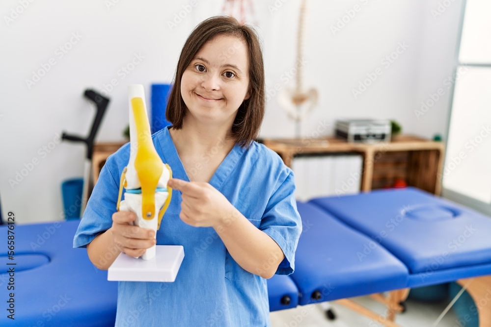 Brunette woman with down syndrome working holding anatomical knee at physiotherapy clinic Brunette woman with down syndrome working holding anatomical knee at physiotherapy clinic