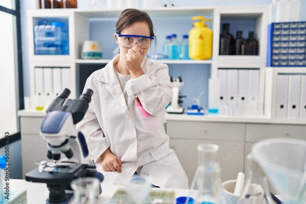 Hispanic girl with down syndrome working at scientist laboratory tired rubbing nose and eyes feeling fatigue and headache. stress and frustration concept. Hispanic girl with down syndrome working at scientist laboratory tired rubbing nose and eyes feeling fatigue and headache. stress and frustration concept.