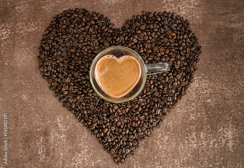 Herzförmige Tasse aus Glas mit Kaffee gefüllt auf einem Herz aus gerösteten Kaffeebohnen vor meliertem hellbraunem Hintergrund, horizontal, Topview   photo