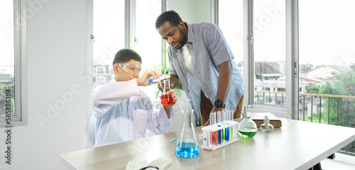 Teacher and child student studying chemical science in classroom. Multiracial male tutor teaching liquid experiment to boy pupil in class. Schoolboy back to school and learning with multiethnic person