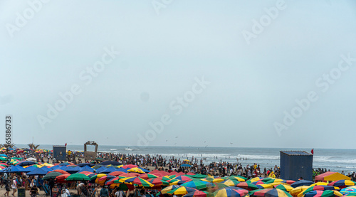 large number of people enjoying the beach under the colorful umbrellas and a good sun next to the pier