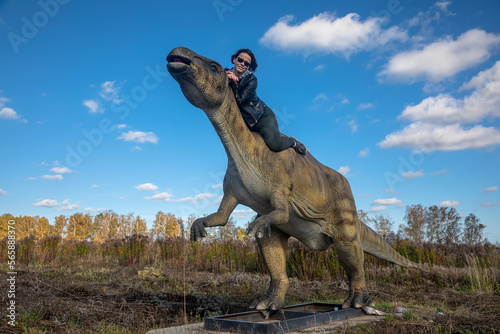 Beautiful girl near the dinosaur. Girl in a leather jacket. Sunny day. Dinosaur in the field.