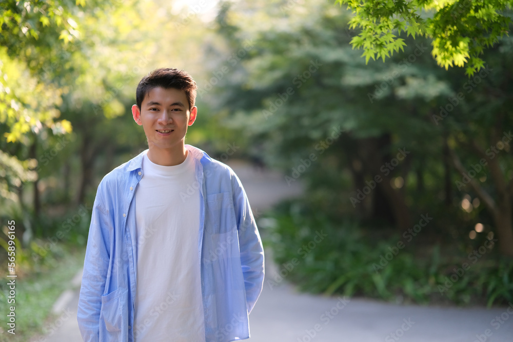 portrait of handsome Chinese young man smile at camera, with green trees under sunshine portrait of handsome Chinese young man smile at camera, with green trees under sunshine