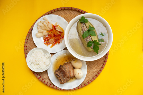 Family dinning table of Tet holiday or Lunar New Year with traditional foods: pork belly and eggs braised in coconut water, pickles, rice, Banh Tet (rice cake), fried vegetables, bitter melon soup
