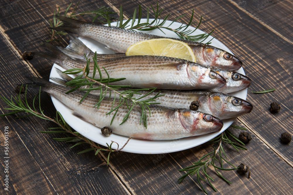 A lot of peeled fresh mullet fish lies on a white plate, surrounded by spices and rosemary sprigs