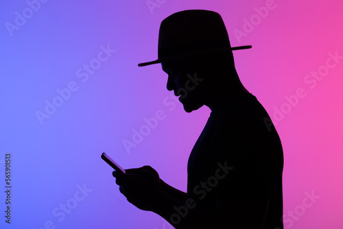 Confident african man silhouette using mobile phone while standing to neon background with copy space