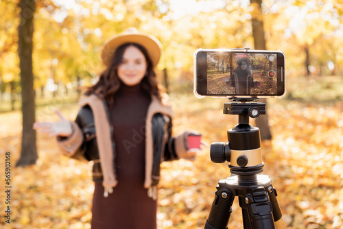 Woman blogger shooting some video on phone screen in park in autumn while traveling.