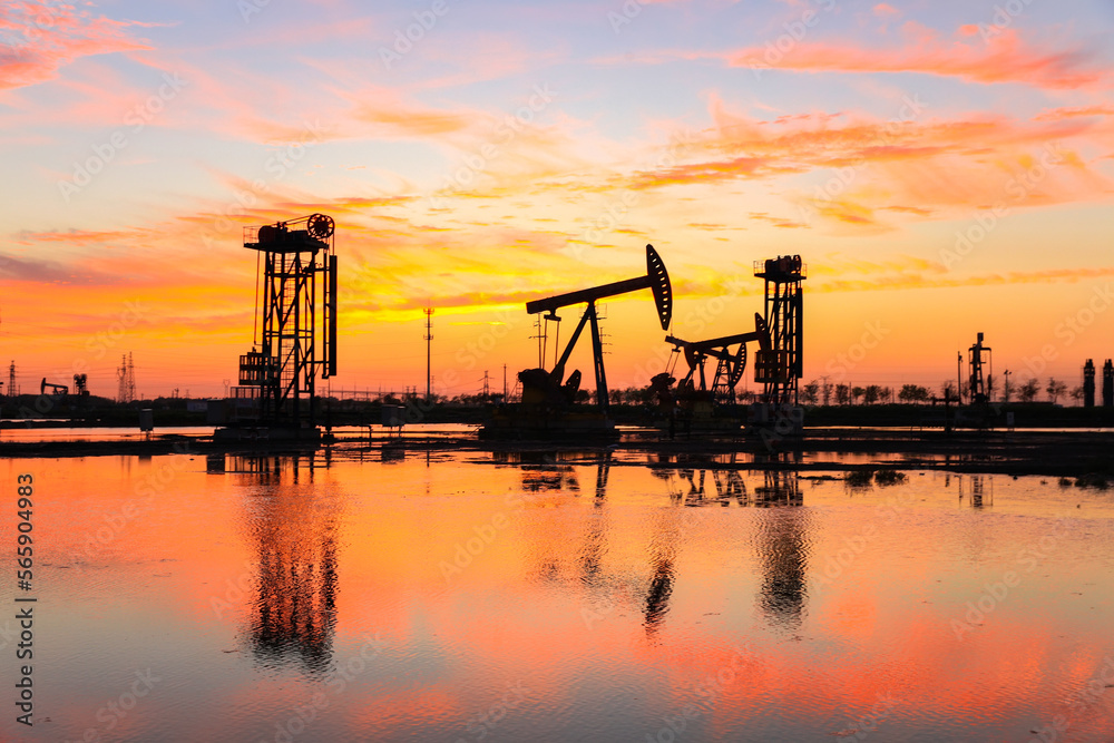 Obraz premium in the evening, oil pumps are running, The oil pump and the beautiful sunset reflected in the water, the silhouette of the beam pumping unit in the evening.