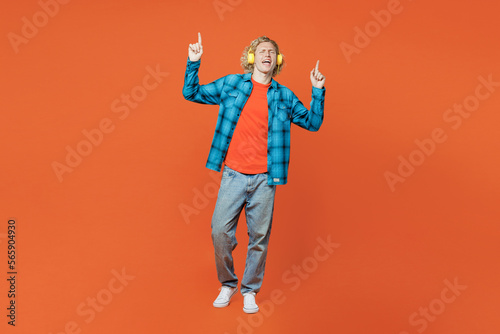Full body young fun cheerful blond man wear blue shirt orange t-shirt headphones listen to music dance gesticulating hands isolated on plain red background studio portrait. People lifestyle concept.