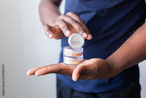 African american man holds mineral facial powder for perfect make-up for women - male make-up artist and cosmetic product concept