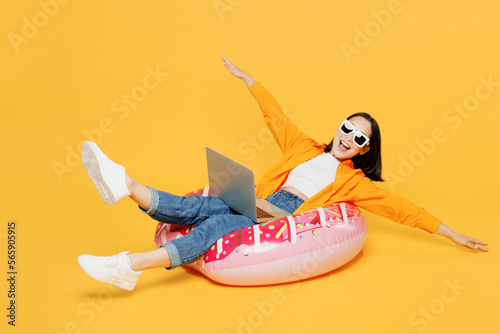 Young woman in summer clothes sit rubber ring use laptop pc computer spread hand isolated on plain yellow background. Tourist travel abroad in free time rest getaway Air flight trip journey concept #565905915