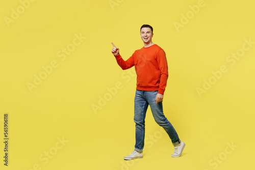 Full body profile young smiling happy cheerful man wear orange casual clothes walking going point index finger aside isolated on plain yellow color background studio portrait People lifestyle concept