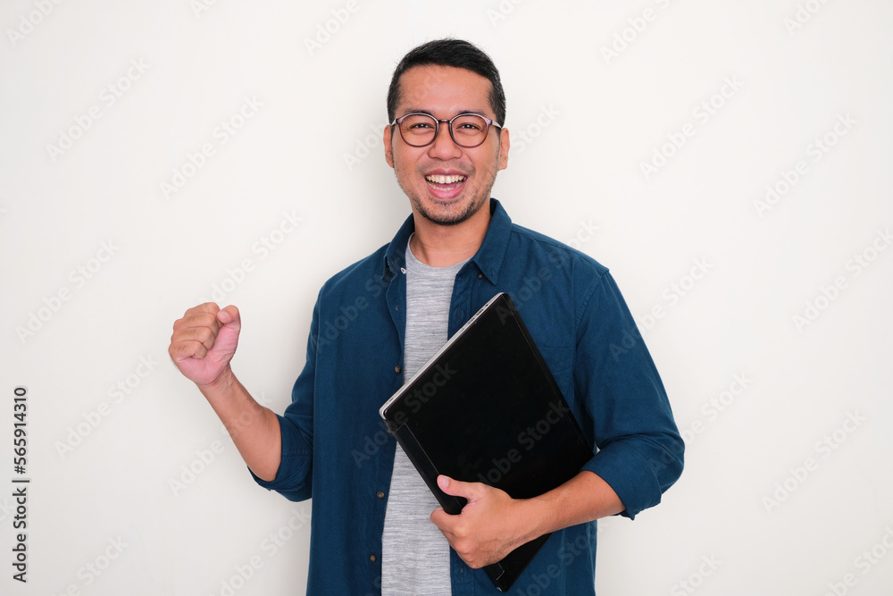 Adult Asian man clenched fist and showing excited while holding a laptop Adult Asian man clenched fist and showing excited while holding a laptop
