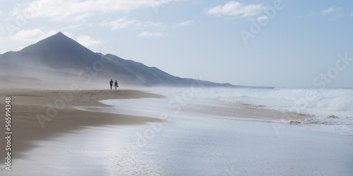 Beach view with waves, fog and sea spray and two people in Cofete Fuerteventura Canary Islands photo