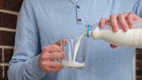 A man pours fresh milk from a bottle into a glass, close-up